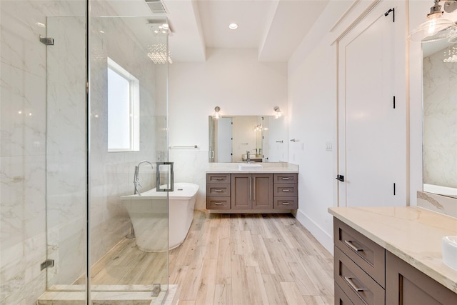 full bathroom featuring a sink, wood finished floors, two vanities, a soaking tub, and a marble finish shower