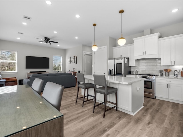 kitchen featuring tasteful backsplash, light stone counters, a center island, stainless steel appliances, and white cabinetry