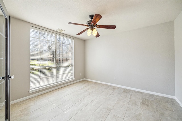 empty room featuring a textured ceiling, a ceiling fan, visible vents, and baseboards