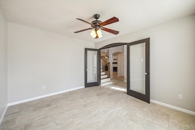 empty room featuring a ceiling fan, arched walkways, french doors, and baseboards