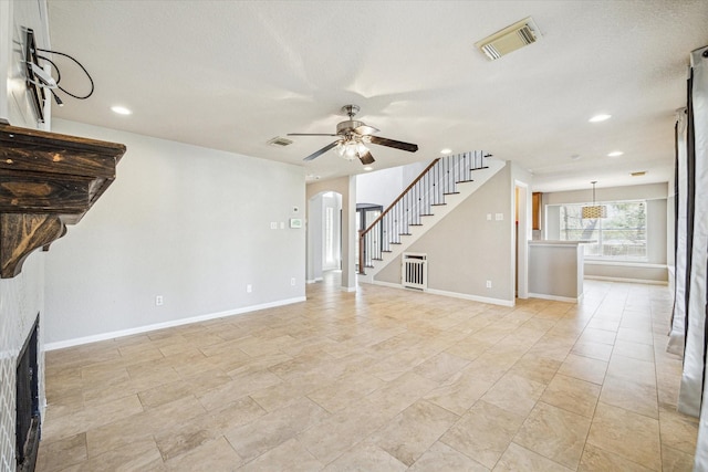 unfurnished living room featuring arched walkways, a fireplace, visible vents, ceiling fan, and stairs