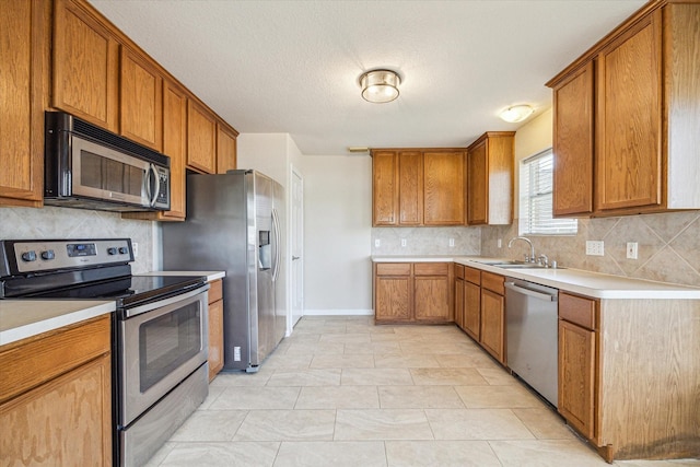 kitchen with a sink, stainless steel appliances, brown cabinetry, and light countertops