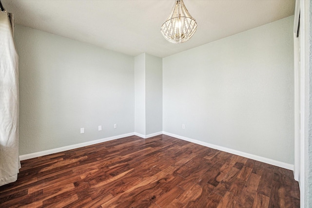 unfurnished room with baseboards, dark wood finished floors, and an inviting chandelier