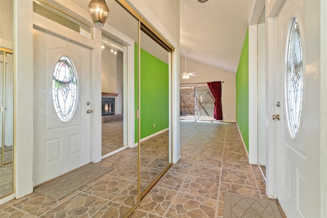 foyer with lofted ceiling, a healthy amount of sunlight, a glass covered fireplace, and stone floors