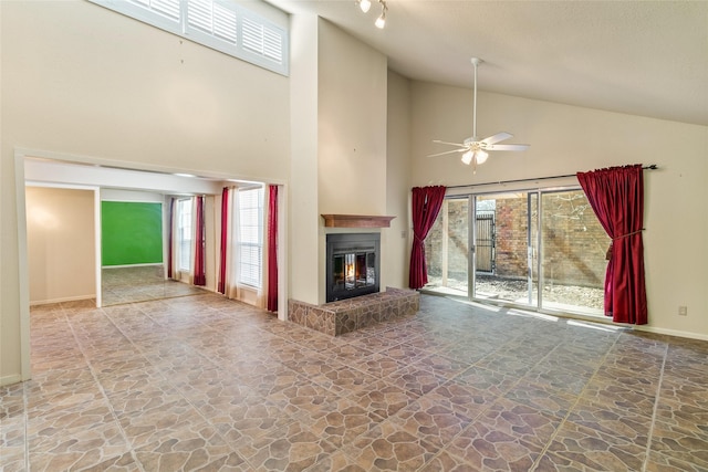 unfurnished living room with stone finish flooring, high vaulted ceiling, a glass covered fireplace, and baseboards