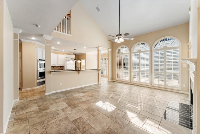 unfurnished living room featuring decorative columns, baseboards, a fireplace, high vaulted ceiling, and ceiling fan with notable chandelier