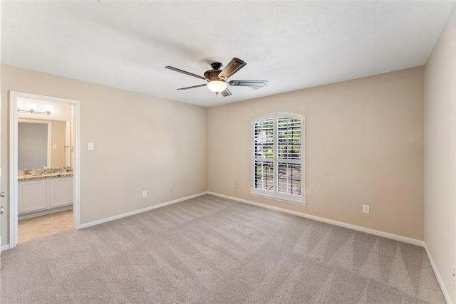 unfurnished bedroom featuring a textured ceiling, connected bathroom, light colored carpet, a ceiling fan, and baseboards