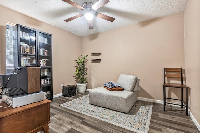 living area with a ceiling fan, a textured ceiling, baseboards, and wood finished floors