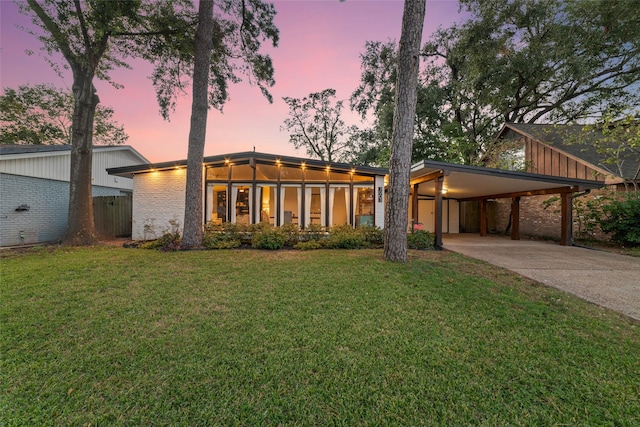 mid-century inspired home featuring brick siding, concrete driveway, a carport, and a front lawn