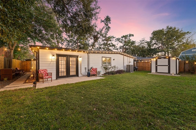 back of property at dusk with french doors, a storage unit, a fenced backyard, and an outdoor structure