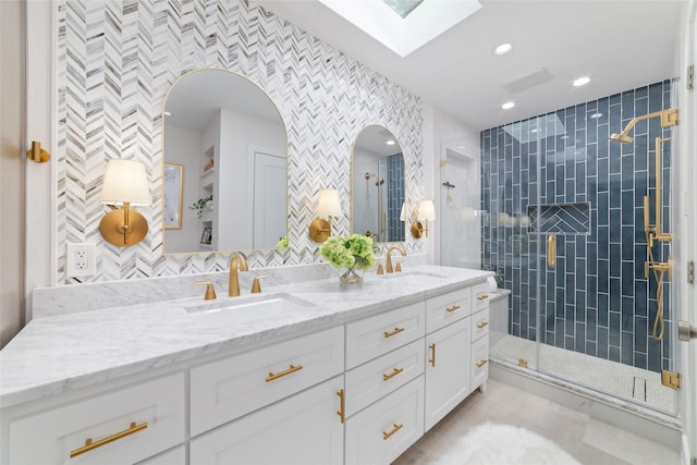 bathroom featuring a sink, a skylight, a stall shower, and double vanity