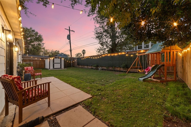 view of yard featuring an outbuilding, a fenced backyard, a storage unit, a playground, and a patio area