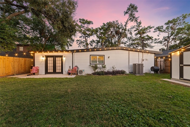 back of property at dusk featuring cooling unit, french doors, a lawn, and a fenced backyard