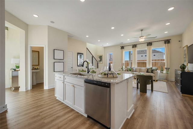 kitchen with light stone counters, light wood finished floors, white cabinets, a sink, and dishwasher