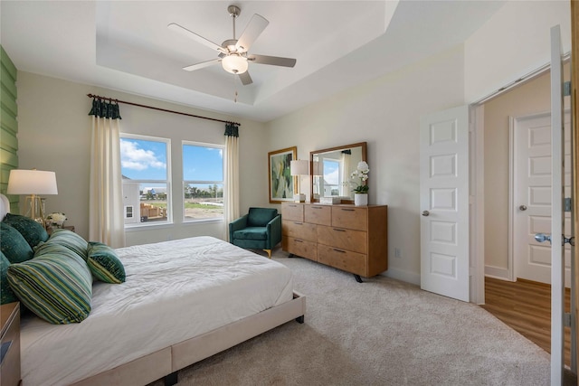 bedroom with baseboards, a raised ceiling, a ceiling fan, and light colored carpet