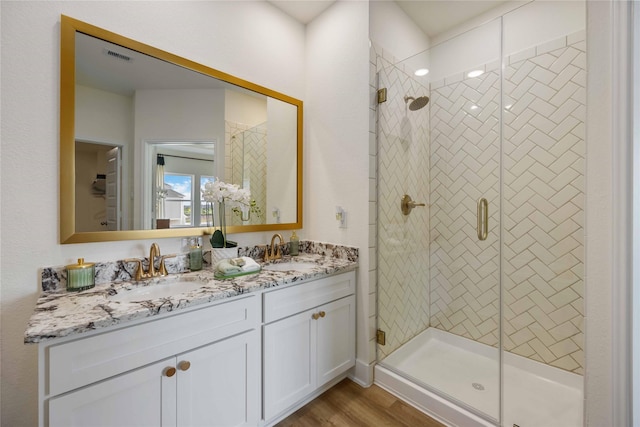 full bath with double vanity, wood finished floors, a sink, and a shower stall