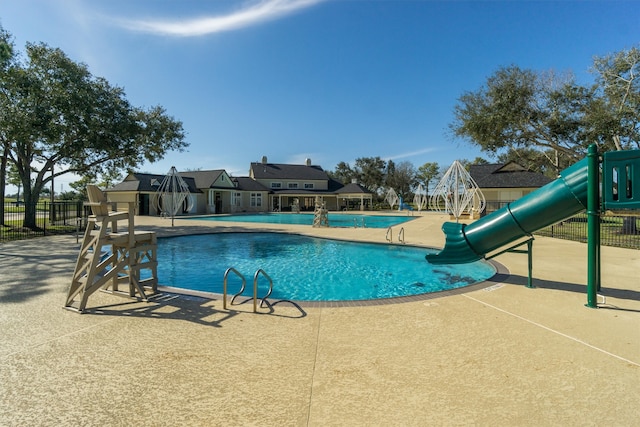 pool featuring a water slide, playground community, fence, and a patio