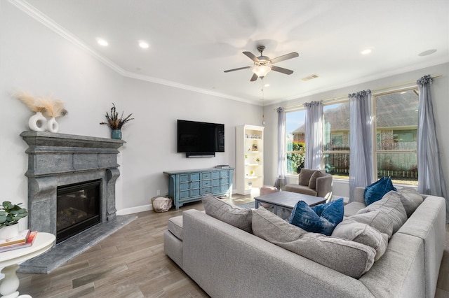 living area with crown molding, visible vents, a glass covered fireplace, wood finished floors, and baseboards