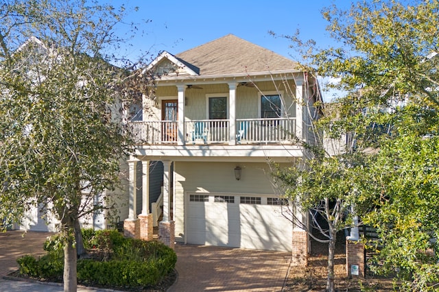 view of front facade featuring decorative driveway, a shingled roof, an attached garage, a ceiling fan, and a balcony