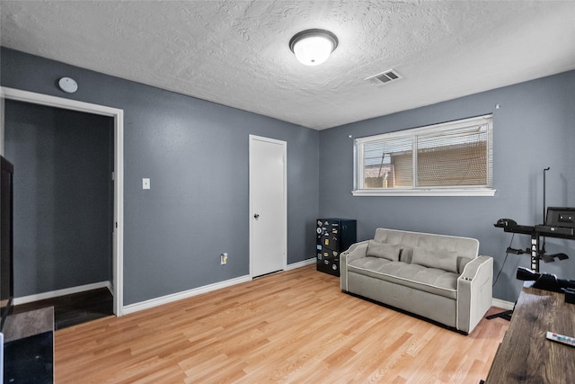 living area featuring a textured ceiling, wood finished floors, visible vents, and baseboards