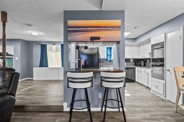 kitchen with visible vents, freestanding refrigerator, white cabinetry, wood finished floors, and a kitchen bar