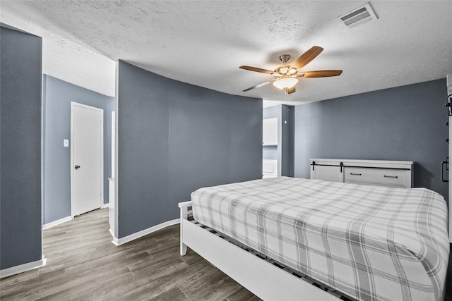 bedroom with a textured ceiling, wood finished floors, a ceiling fan, visible vents, and baseboards