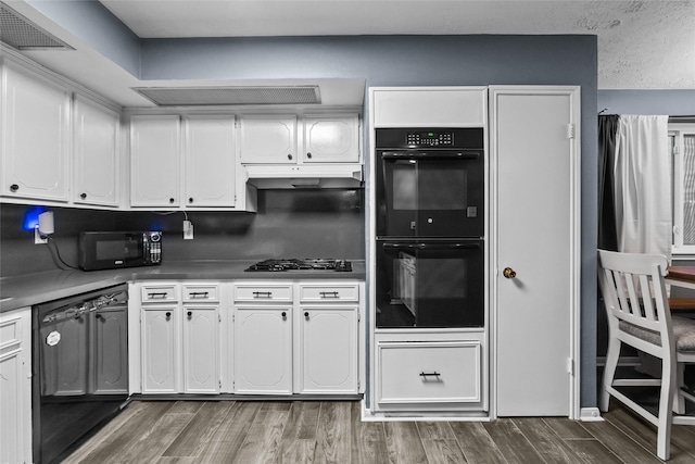 kitchen featuring under cabinet range hood, wood finished floors, white cabinetry, visible vents, and black appliances