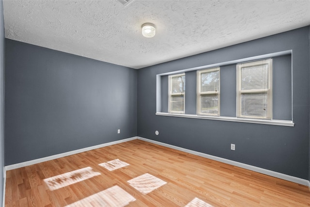 empty room with a textured ceiling, baseboards, and wood finished floors