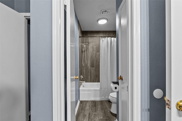 bathroom featuring wood finish floors, visible vents, a textured wall, toilet, and shower / bath combo with shower curtain