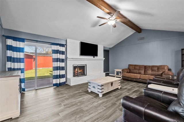 living room with vaulted ceiling with beams, a fireplace, visible vents, a ceiling fan, and wood finished floors