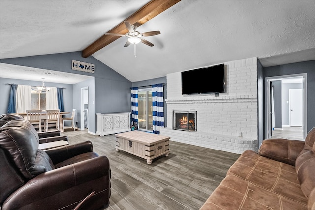 living area featuring lofted ceiling with beams, a brick fireplace, a textured ceiling, wood finished floors, and ceiling fan with notable chandelier