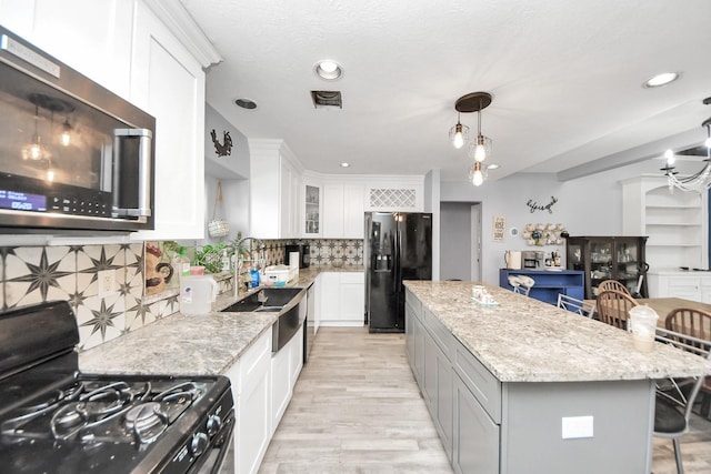 kitchen featuring light stone counters, a kitchen breakfast bar, white cabinets, a center island, and black appliances