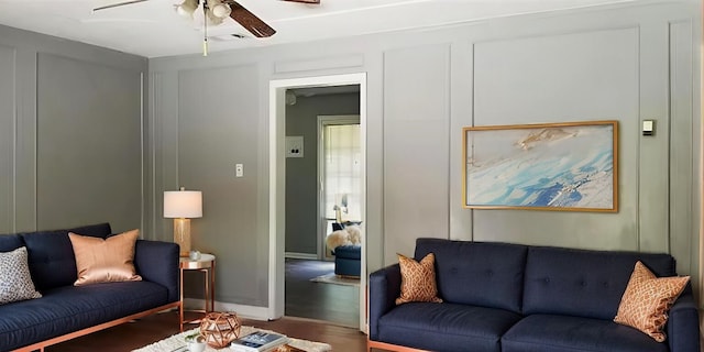 living room with ceiling fan, wood finished floors, visible vents, and a decorative wall