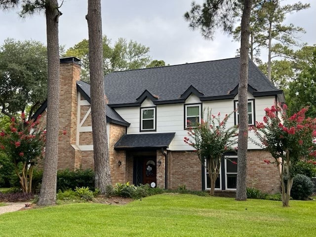 traditional home with a shingled roof, a chimney, a front lawn, and brick siding