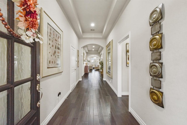 corridor with baseboards, arched walkways, dark wood-style floors, a tray ceiling, and recessed lighting