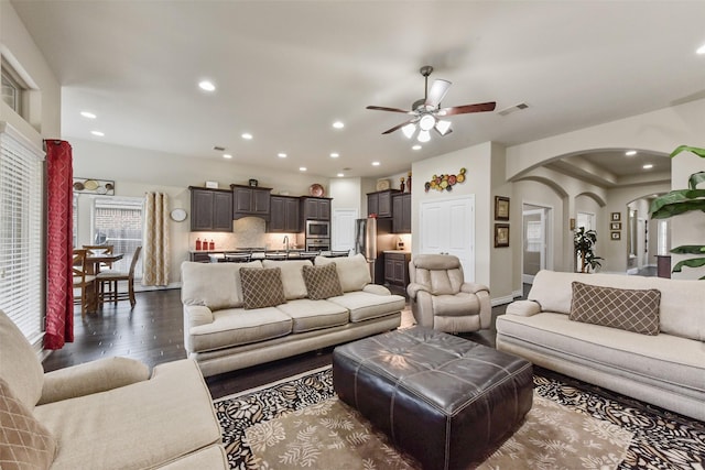 living room with arched walkways, recessed lighting, dark wood-type flooring, a ceiling fan, and visible vents