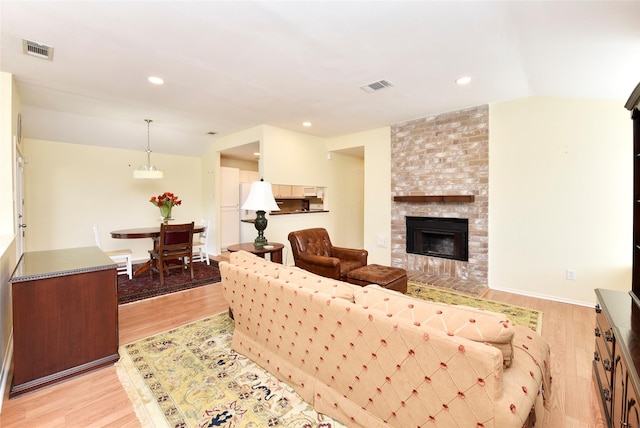 living room with light wood-type flooring, a brick fireplace, visible vents, and recessed lighting