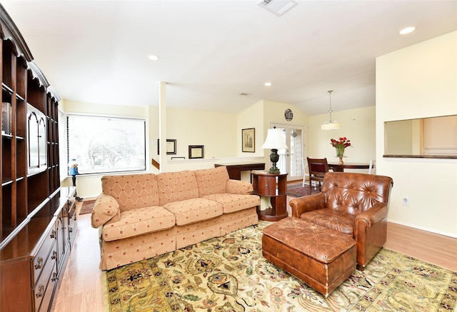 living area with vaulted ceiling, plenty of natural light, wood finished floors, and visible vents