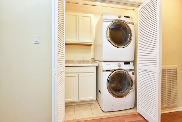 washroom featuring light tile patterned flooring, stacked washing maching and dryer, cabinet space, and visible vents