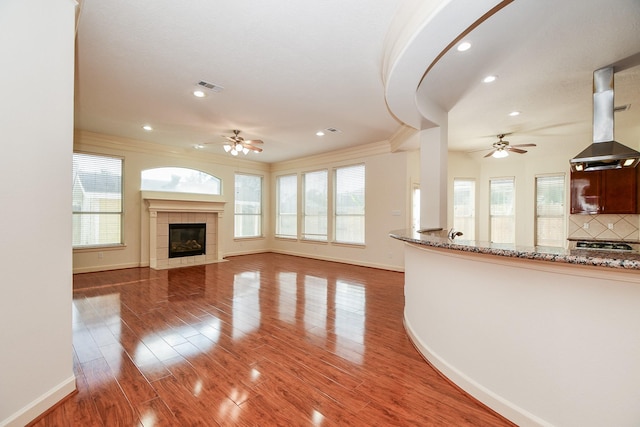 unfurnished living room with ceiling fan, a tiled fireplace, visible vents, and wood finished floors