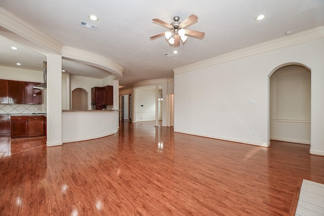 unfurnished living room featuring arched walkways, crown molding, visible vents, ceiling fan, and wood finished floors