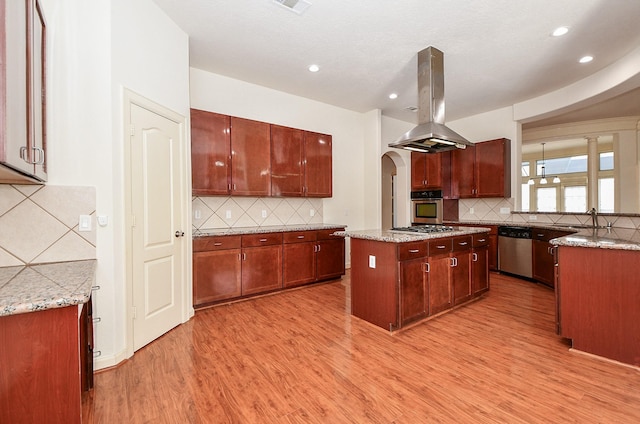 kitchen with island range hood, arched walkways, light wood-style flooring, a center island, and stainless steel appliances