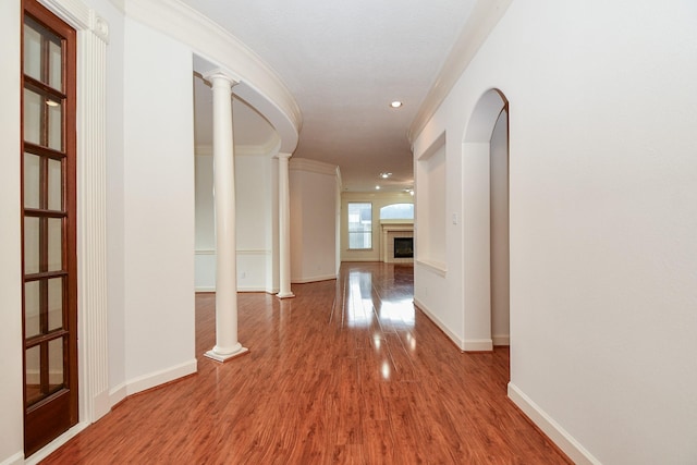 hallway featuring crown molding, wood finished floors, decorative columns, and baseboards