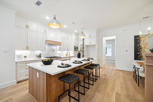 kitchen with light wood finished floors, custom range hood, visible vents, and a sink