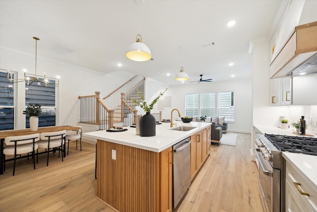 kitchen featuring a kitchen island with sink, premium range hood, a sink, appliances with stainless steel finishes, and light wood finished floors