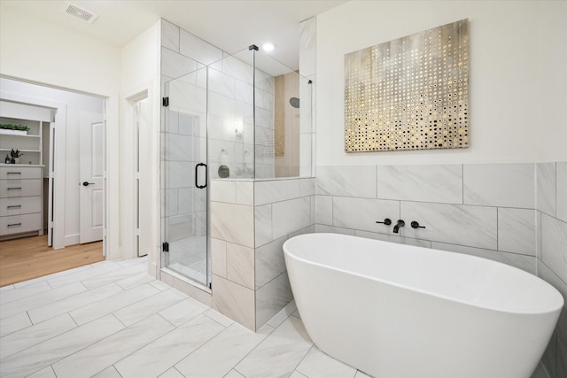 bathroom with a soaking tub, a shower stall, visible vents, and tile walls