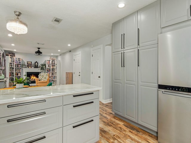 walk in closet featuring a warm lit fireplace, light wood-style flooring, and visible vents