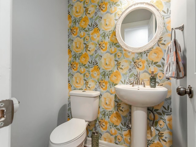 half bathroom with baseboards, toilet, and wallpapered walls