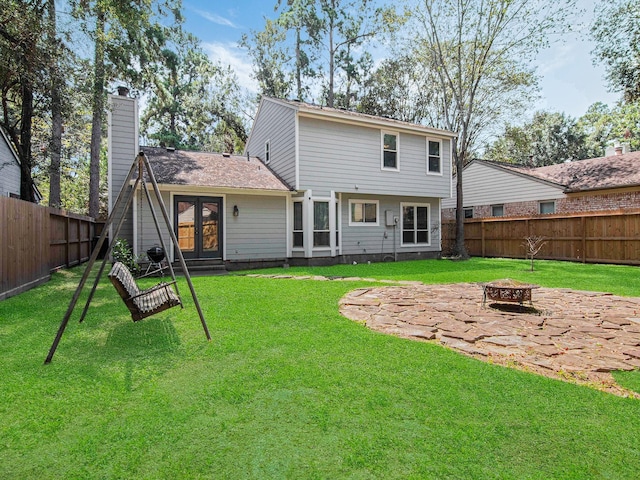 rear view of house with a yard, an outdoor fire pit, a fenced backyard, and french doors