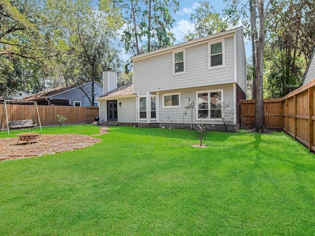 back of house featuring a fenced backyard, a chimney, a fire pit, and a yard